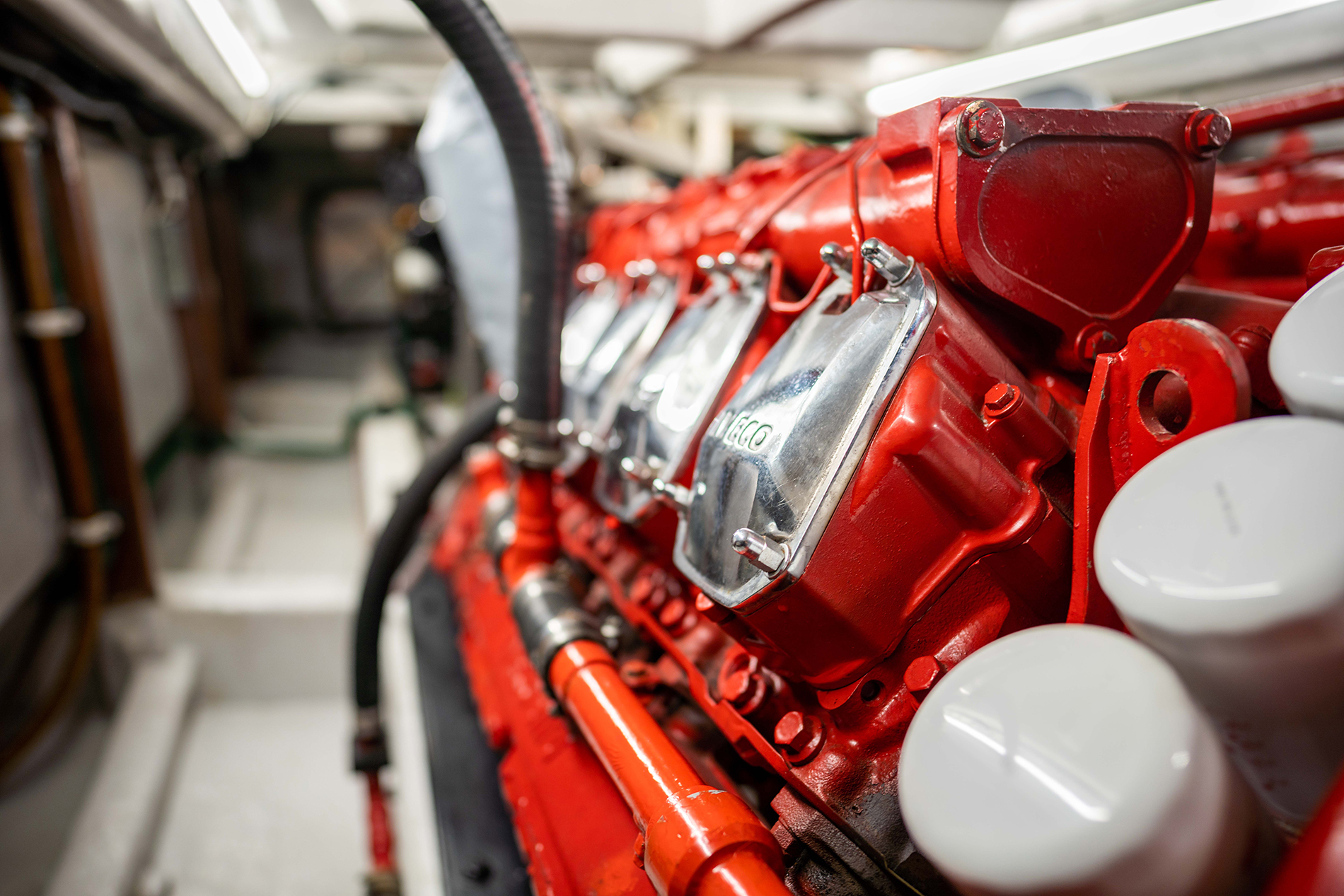 Close-up view of a shiny, red-painted industrial engine with metallic components and pipes, taken in a well-lit, confined mechanical room—ideal for Maritime & Defense applications. The focus is on the glossy metal casings and detailed engine parts.
